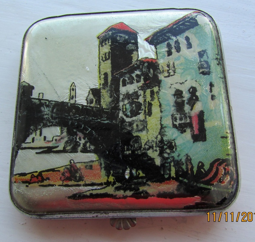 Small square compact with polished metal mirror and sifter in place. The picture is showing tall buildings and a bridge. The coral coloured back has small sratches but the front is perfect. A very pretty compact.