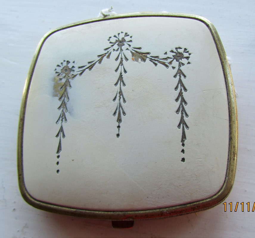This small cream-coloured compact is of good quality. There is a polished metal mirror that lifts to reveal a rouge well and a powder well. The back of the compact is cream and there is lovely scrolling to the edges.